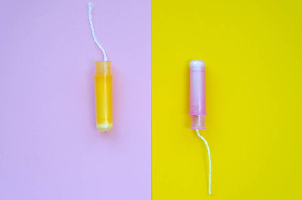 Two hygiene tampons with applicator on pink and yellow background. Hygiene products for women's monthly menstruation. Protection tampons for female health. Copy space. Top view. Flat lay - Fotó, kép