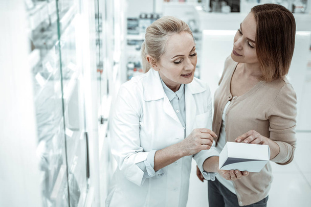 A pleasing druggist advising the female customer on vitamins ingredients - Фото, зображення