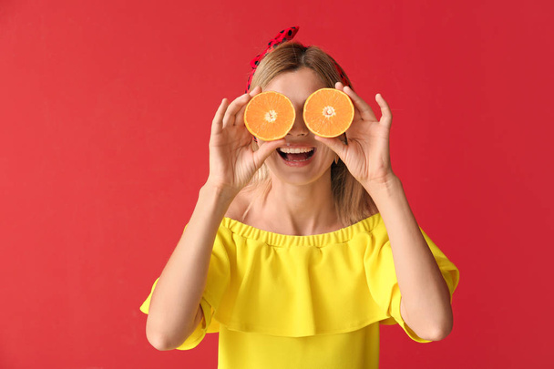 Happy beautiful woman with orange fruit on color background - Foto, afbeelding