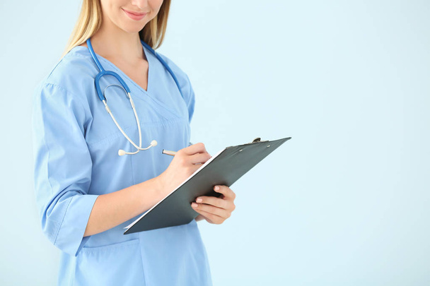 Female nurse with stethoscope and clipboard on color background - Fotoğraf, Görsel
