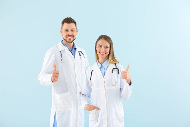 Mannelijke en vrouwelijke artsen tonen duim-up op lichte kleur achtergrond - Foto, afbeelding