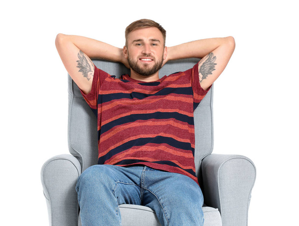 Komea nuori mies rentouttava nojatuoli valkoista taustaa vasten
 - Valokuva, kuva