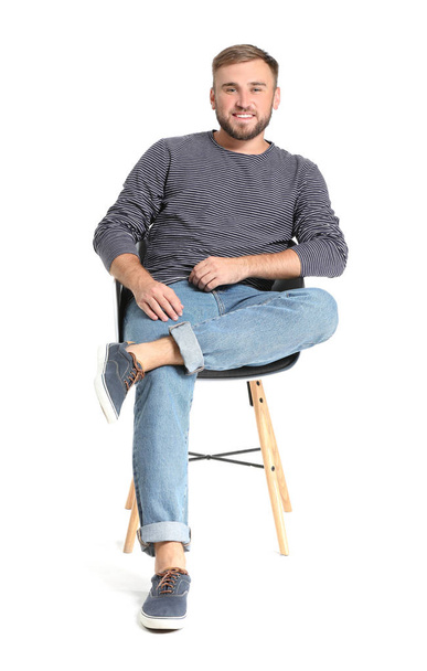 Όμορφος νέος άντρας που κάθεται στην καρέκλα ενάντια στο λευκό φόντο - Φωτογραφία, εικόνα