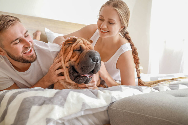 Ευτυχισμένο ζευγάρι με χαριτωμένο σκυλί στο κρεβάτι στο σπίτι - Φωτογραφία, εικόνα