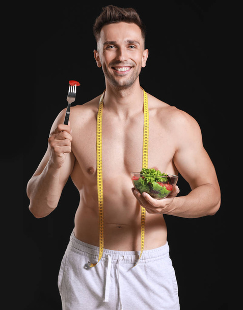 Koyu arka planda ölçüm bandı ve salata ile Yakışıklı kaslı adam. Kilo kaybı kavramı - Fotoğraf, Görsel