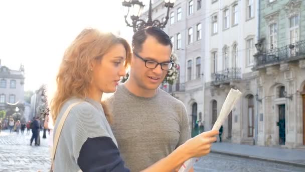 Νεαρό ζευγάρι βλέποντας τον χάρτη της πόλης και ψάχνοντας για κατεύθυνση νωρίς το πρωί σε άδεια αρχαία πλατεία κάπου στην Ευρώπη, ταξιδεύοντας concept - Πλάνα, βίντεο