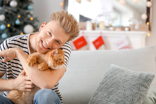 Mladý muž s roztomilou kočkou doma na Štědrý den - Fotografie, Obrázek