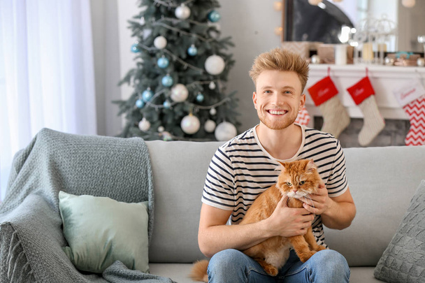 Jonge man met schattige kat thuis op kerstavond - Foto, afbeelding