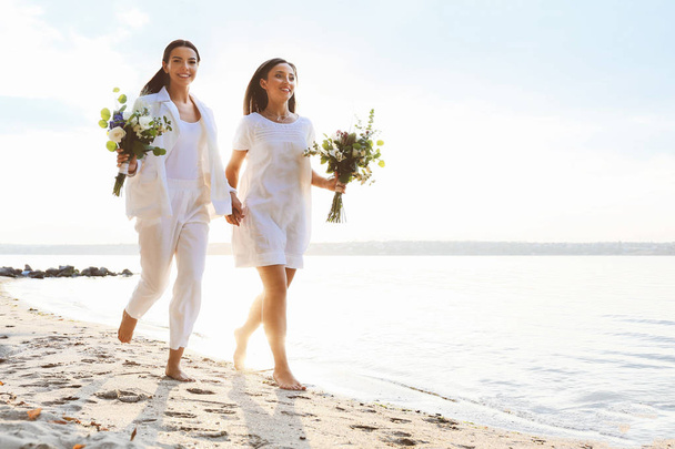 Beautiful lesbian couple walking along a river bank on their wedding day - Photo, Image