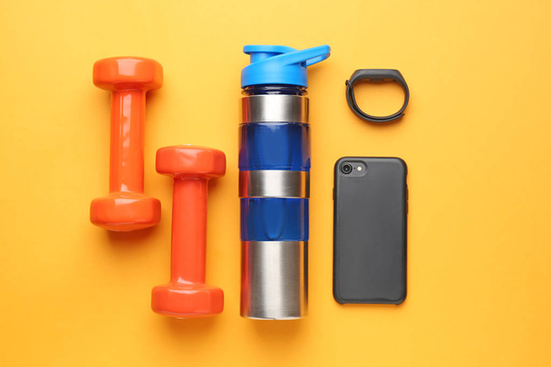 Бутылка спортивной воды, гантели, мобильный телефон и фитнес-трекер на цветном фоне
 - Фото, изображение