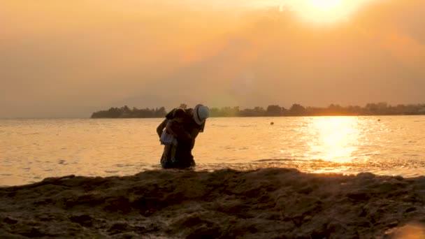 Vader speelt met dochter op het strand tijdens zonsondergang. Gelukkig ouderschap concept. Abstracte achtergrond. Zomer vakantie met kind. Gelukkige vader met vrolijke jongen op handen met zonsondergang achtergrond - Video