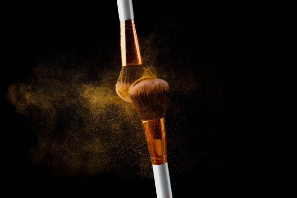 Cosmetic brush with golden powder spreading on black background - Foto, immagini