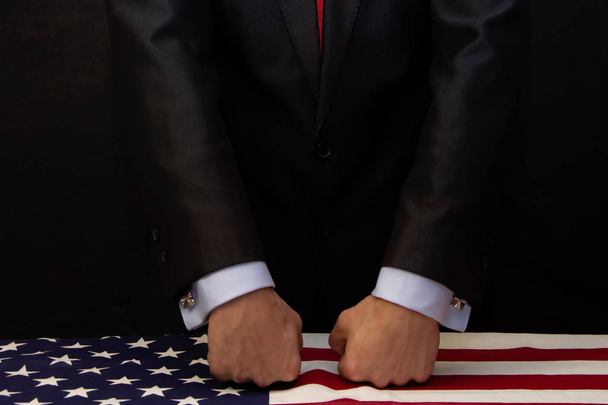 The man puts his fists on the table covered with the American flag. Concept: conflict, force, revenge and offense, threat - Foto, Bild