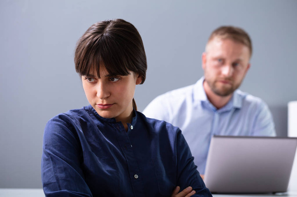 Angry Businesswoman Sitting In Front Of Businessman With Laptop Looking At Her Against Grey Background - Photo, Image