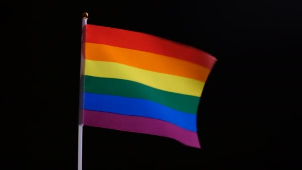Un drapeau orgueilleux aux couleurs arc-en-ciel oscille dans le vent. Drapeau LGBT sur fond noir. Symbole d'indépendance et d'amour entre personnes de même sexe. Zoom avant et arrière en douceur. Le concept des minorités sexuelles
. - Séquence, vidéo