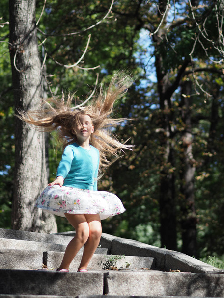 щаслива і весела дівчина у відпустці в парку 9 років з довгим світлим волоссям, яке розвивається під час стрибка
 - Фото, зображення