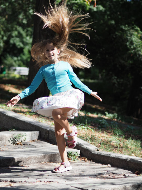 ευτυχισμένο και χαρούμενο κορίτσι σε διακοπές στο πάρκο 9 χρόνια με μακριά ξανθά μαλλιά που αναπτύσσεται κατά τη διάρκεια του άλματος - Φωτογραφία, εικόνα