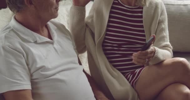 Front view close up of a senior Caucasian woman and man sitting on a couch and using a smartphone - Video