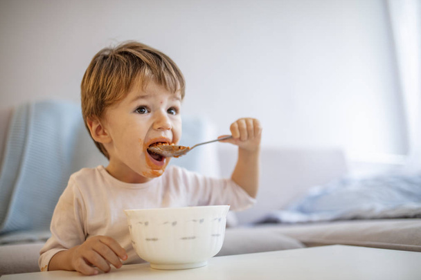 Cute child eating healthy food with with the left hand at home. Cute child little boy eats healthy food vegetables. It's really yummy. Kid eating healthy food at home or kindergarten - Fotoğraf, Görsel