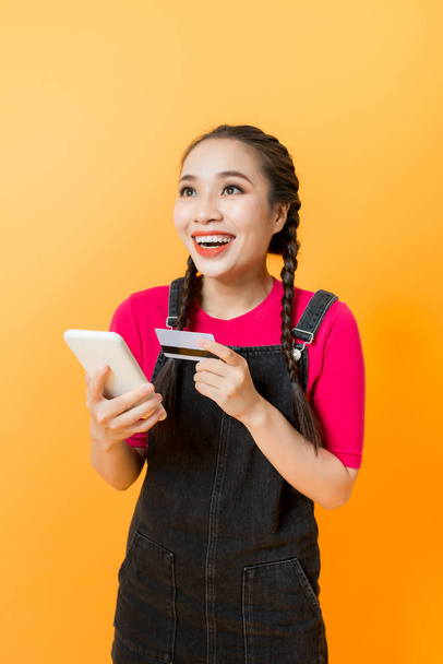 Asian woman use smartphone to payment online shopping with blank credit card, yellow background - Photo, Image