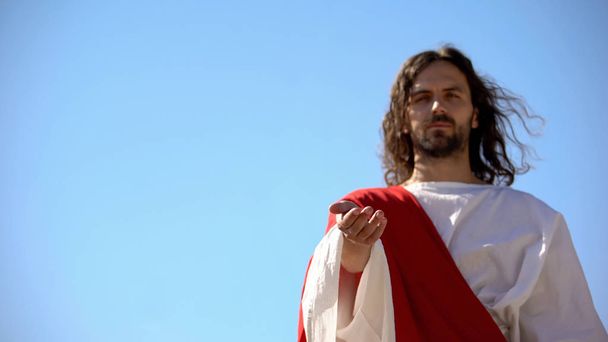Jesus reaching out hand against blue sky, forgiveness and salvation of sinners - 写真・画像