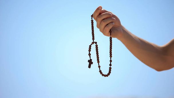 Hand holding rosary, praying to god on blue background, religious spirituality - Valokuva, kuva