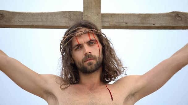 Jesus suffering nailed to cross, looking into camera, sacrifice for sinners - Foto, imagen
