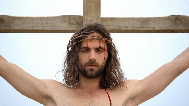 Jesus crucified on wooden cross, bloody head with crown of thorns, sacrifice - Fotó, kép