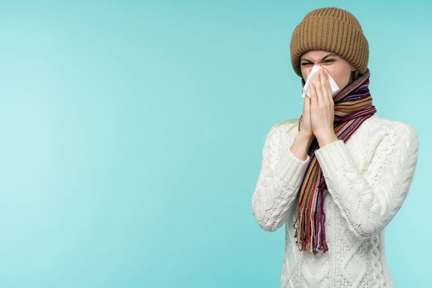 Health and medicine concept - Young woman blowing nose into tissue, on a blue background. Pretty girl cold with snot. - Foto, immagini