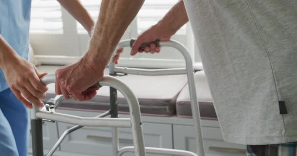 Side view close up of a senior Caucasian man using a walking frame and young Caucasian female doctor in a hospital - Πλάνα, βίντεο