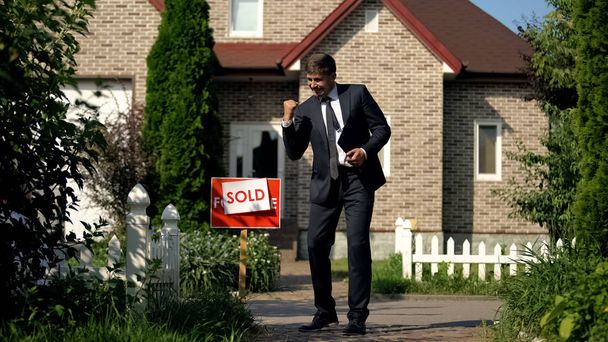 Agent immobilier en costume d'affaires montrant oui geste debout devant la maison vendue
 - Photo, image