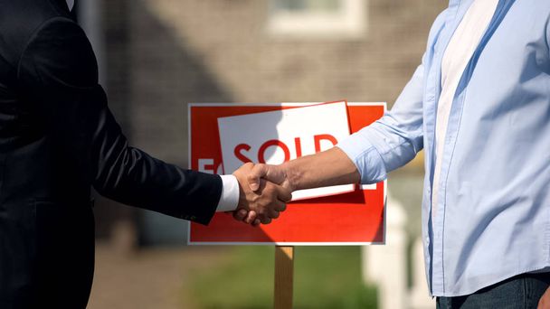 Real estate broker and new house owner shaking hands in front of sold signboard - Фото, зображення