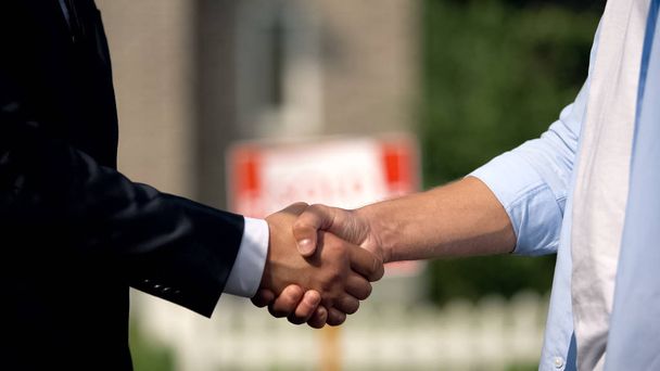 Dos hombres estrechando las manos en el fondo de letrero vendido, compra de casa exitosa
 - Foto, Imagen