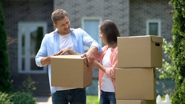 Happy couple sorting cardboard boxes in front of new house, moving concept - Foto, Imagem