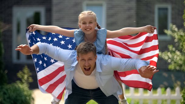 Excited dad and girl patriots having fun, holding USA flag, family immigration - Foto, Imagen