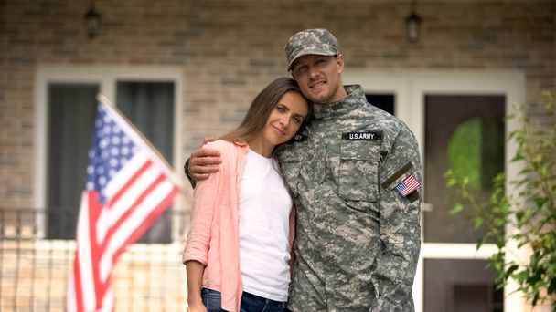 Former soldier and girlfriend hugging, standing against USA flag, homecoming - 写真・画像