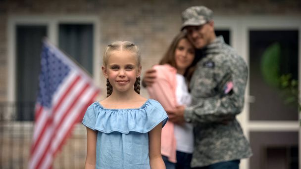 Little girl smiling, american flag strike in front of parents, patriots family - Photo, image