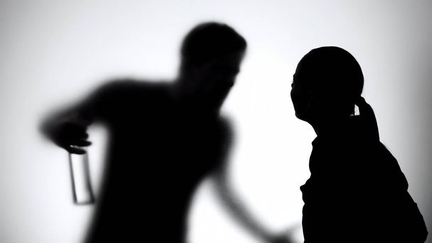 Silhouette of wife and husband quarreling, man holding alcohol bottle, addiction - Fotografie, Obrázek