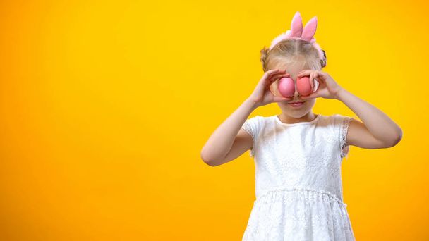 Smiling little girl holding colored eggs in front eyes, Happy Easter greetings - Photo, image