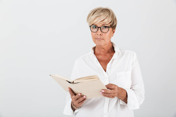 Portrait of adult woman wearing eyeglasses holding book and looking at camera - Foto, imagen