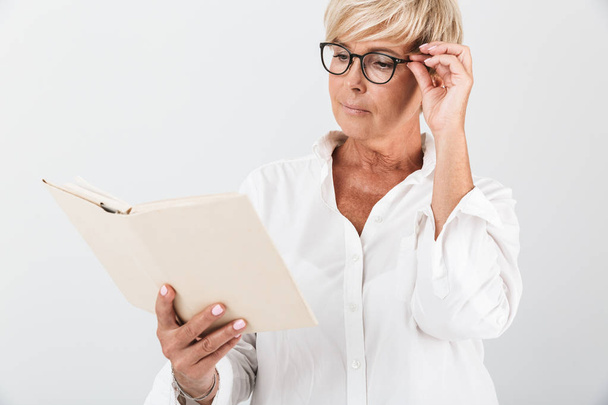 Portrait of focused adult woman wearing eyeglasses reading book - Fotó, kép
