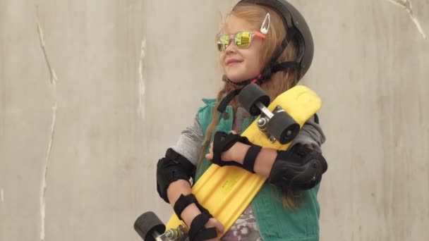 ein fröhliches kleines Mädchen steht mit einem gelben Schlittschuh in der Hand und lächelt - Filmmaterial, Video
