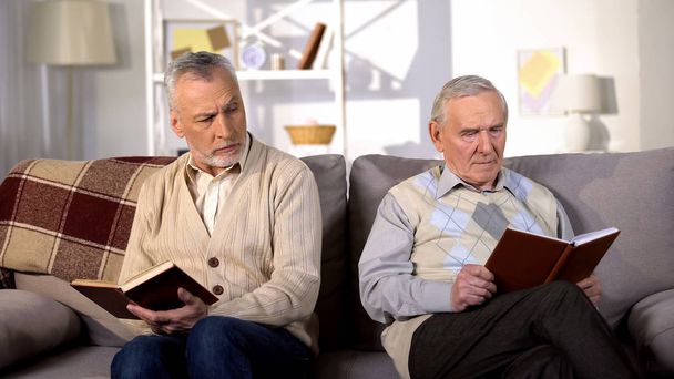 Two offended male friends reading books on sofa home, misunderstanding conflict - Фото, зображення