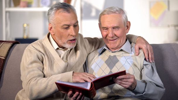 Happy senior brothers watching family album on home sofa, pleasant memories - Foto, immagini