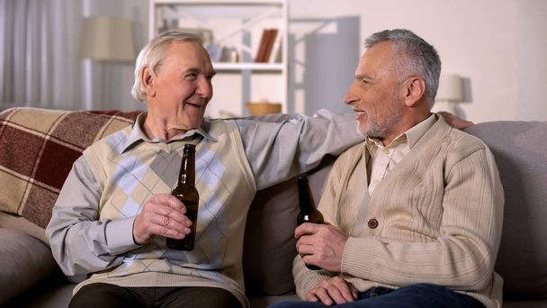 Old friends holding beer bottles, leisure time at home, having fun together - Foto, Imagen
