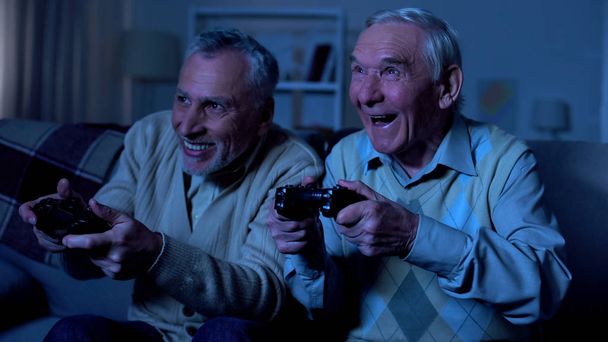 Emotional elderly male friends holding joysticks playing video game, having fun - Zdjęcie, obraz
