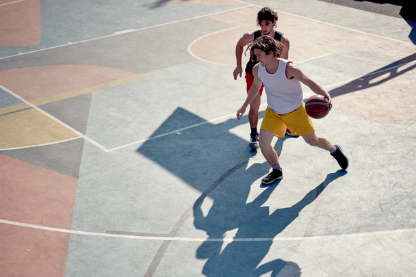 Top view of two young sporty men playing basketball on playground in morning . - Photo, Image