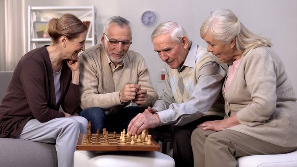 Senior friends playing chess at home, retirement leisure time, togetherness - Foto, afbeelding