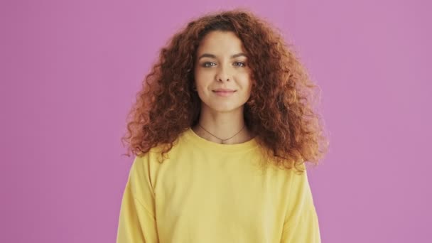 Happy young redhead curly woman smiling while looking at the camera over pink background isolated - Кадры, видео