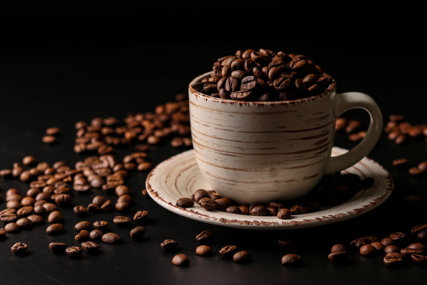 Tasse voller Kaffeebohnen auf dunklem Hintergrund mit verstreuten Kaffeebohnen, horizontale Ausrichtung, Kopierraum - Foto, Bild